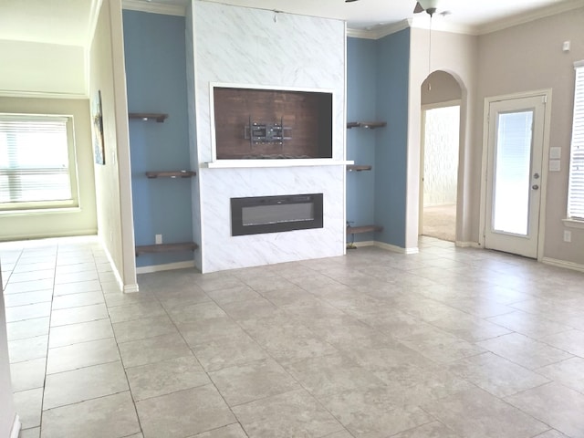 unfurnished living room with ceiling fan, ornamental molding, a premium fireplace, and light tile patterned floors