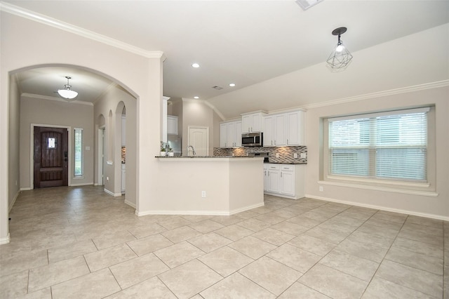 kitchen with tasteful backsplash, vaulted ceiling, hanging light fixtures, ornamental molding, and white cabinets