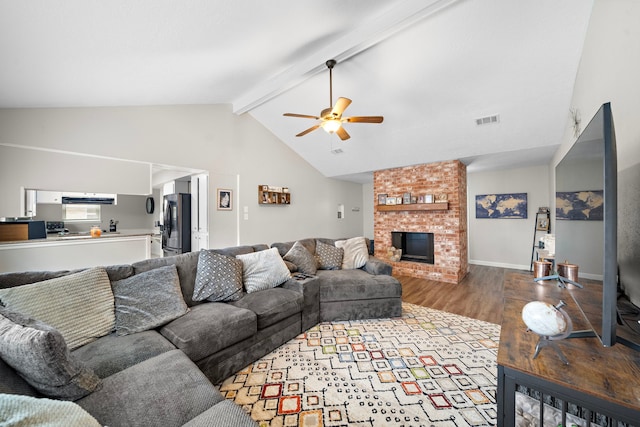 living room with high vaulted ceiling, beamed ceiling, hardwood / wood-style flooring, ceiling fan, and a brick fireplace