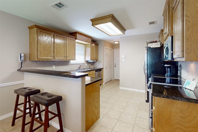 kitchen with stainless steel appliances, a kitchen bar, decorative backsplash, kitchen peninsula, and dark stone counters