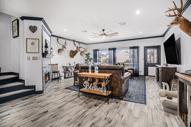 living room featuring ornamental molding, light hardwood / wood-style flooring, a tile fireplace, and ceiling fan