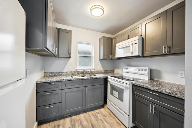 kitchen featuring white appliances, dark stone counters, light hardwood / wood-style floors, and sink