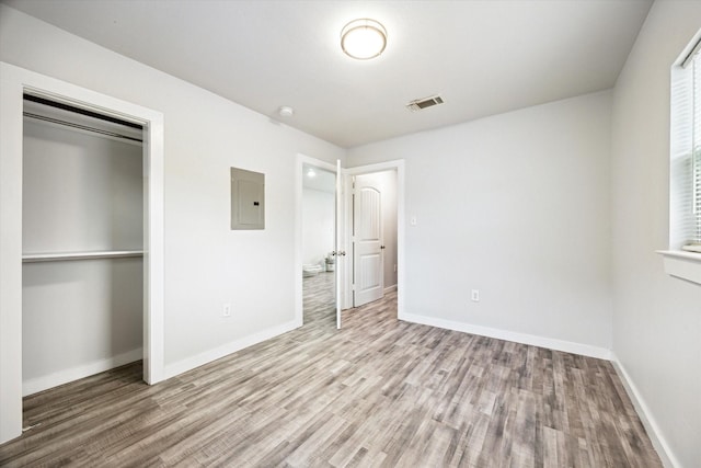 unfurnished bedroom with electric panel, light wood-type flooring, and a closet