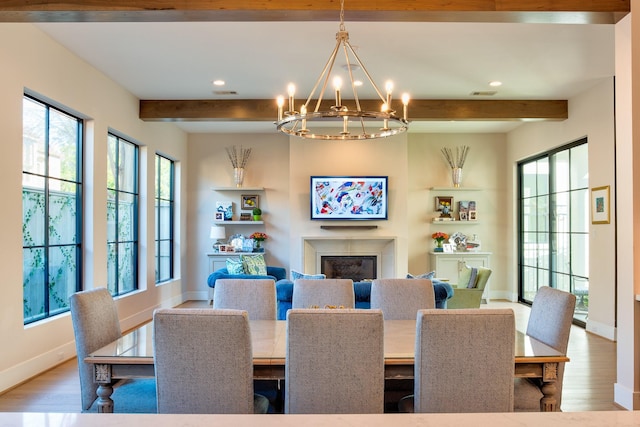 dining area with beamed ceiling, light wood-type flooring, a glass covered fireplace, and an inviting chandelier