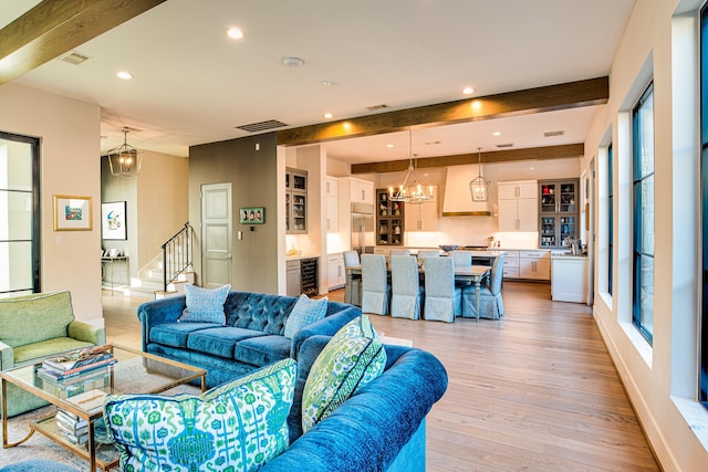 living room featuring a chandelier, beverage cooler, beamed ceiling, and light wood-style floors