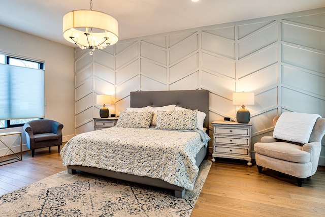 bedroom with light wood-style floors, a decorative wall, and an inviting chandelier