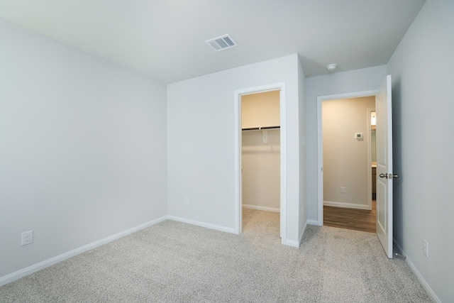 unfurnished bedroom with visible vents, a walk in closet, a closet, carpet flooring, and baseboards