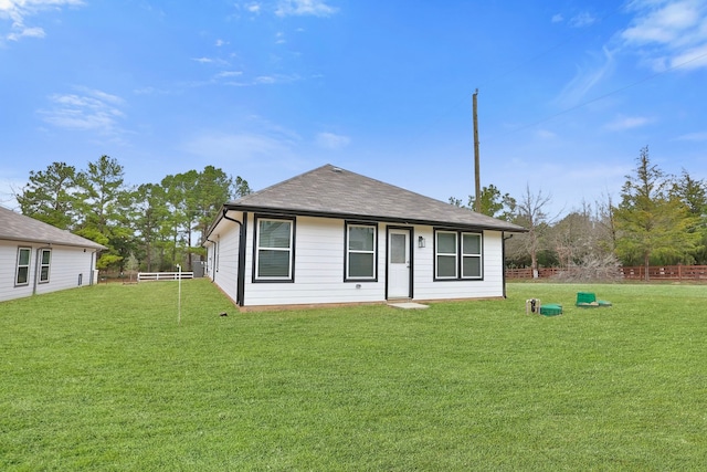 back of house featuring a yard, fence, and roof with shingles