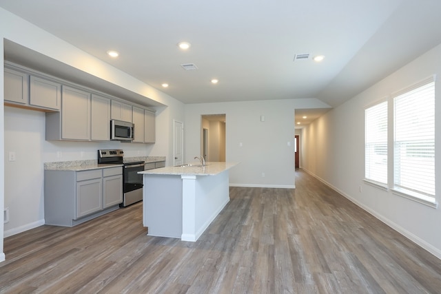 kitchen with visible vents, gray cabinetry, a center island with sink, a sink, and appliances with stainless steel finishes
