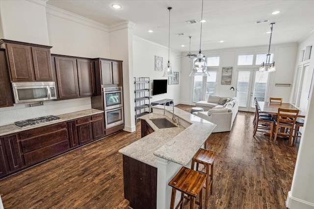 kitchen featuring a kitchen bar, light stone counters, pendant lighting, stainless steel appliances, and a kitchen island with sink