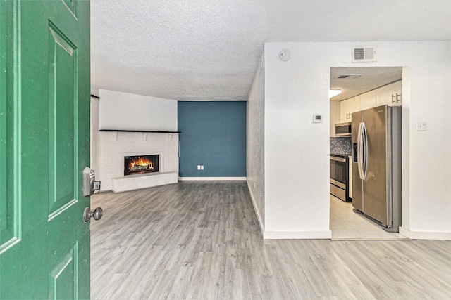 unfurnished living room featuring a brick fireplace, light hardwood / wood-style floors, and a textured ceiling