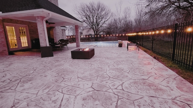 patio terrace at dusk with a fenced in pool, french doors, and an outdoor fire pit