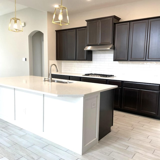 kitchen featuring stainless steel gas cooktop, under cabinet range hood, a sink, and pendant lighting