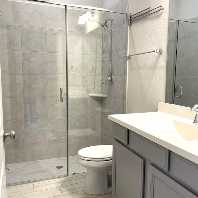 full bath with toilet, a shower stall, vanity, and a textured wall