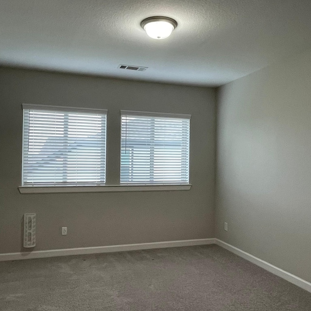 carpeted spare room featuring baseboards, visible vents, and a healthy amount of sunlight