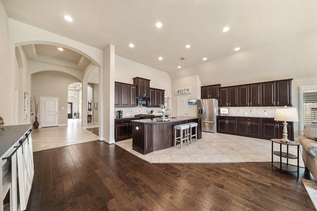 kitchen featuring an island with sink, a breakfast bar area, a high ceiling, stainless steel fridge with ice dispenser, and dark brown cabinets