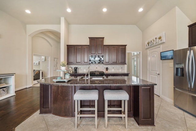 kitchen featuring dark stone countertops, a kitchen island with sink, sink, and stainless steel fridge with ice dispenser