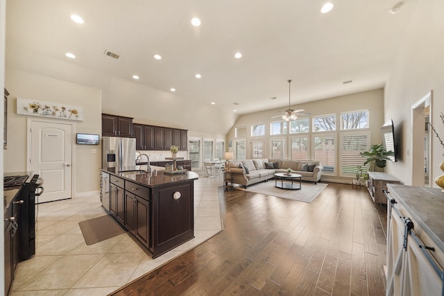 kitchen with black gas range oven, stainless steel fridge, dark brown cabinets, plenty of natural light, and an island with sink