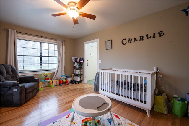 bedroom featuring ceiling fan, wood-type flooring, and a crib