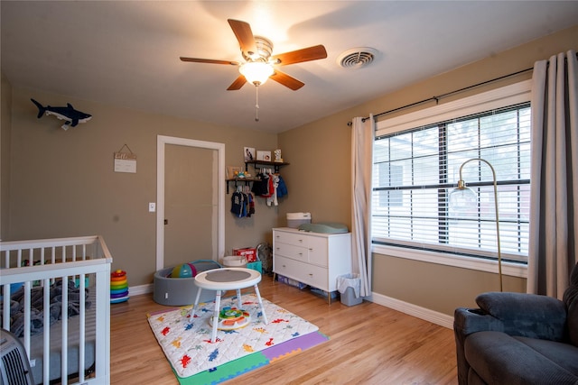 bedroom featuring a nursery area, ceiling fan, and light hardwood / wood-style floors