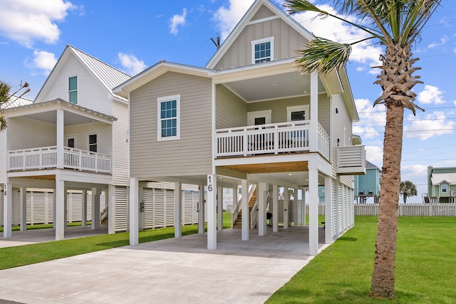 raised beach house featuring a carport, concrete driveway, board and batten siding, and a front yard