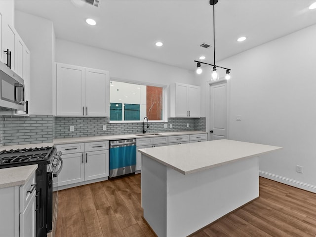 kitchen featuring sink, white cabinetry, hanging light fixtures, stainless steel appliances, and a center island