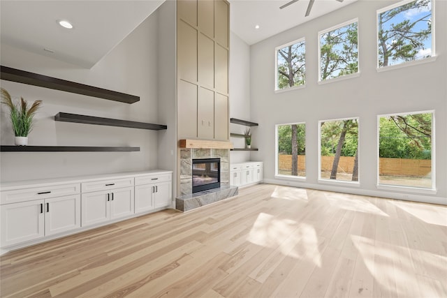 unfurnished living room with a high end fireplace, light hardwood / wood-style flooring, and a high ceiling