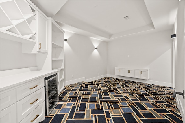 spacious closet featuring beverage cooler, a raised ceiling, and dark colored carpet