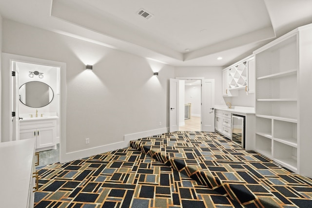 interior space featuring sink, a tray ceiling, beverage cooler, and dark colored carpet