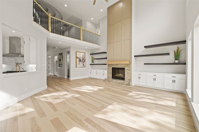 unfurnished living room featuring ceiling fan, a stone fireplace, light hardwood / wood-style flooring, and a high ceiling