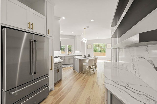 kitchen featuring pendant lighting, white cabinetry, gray cabinetry, high end refrigerator, and light stone counters