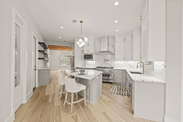 kitchen featuring wall chimney exhaust hood, sink, a center island, appliances with stainless steel finishes, and white cabinets