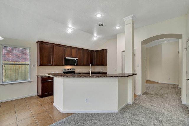 kitchen with lofted ceiling, appliances with stainless steel finishes, dark brown cabinets, tasteful backsplash, and a center island with sink