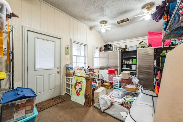 misc room featuring lofted ceiling, concrete flooring, a textured ceiling, wooden walls, and ceiling fan