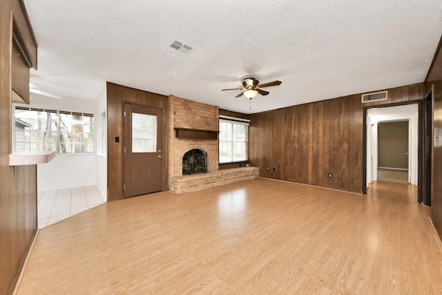 unfurnished living room featuring a fireplace, light hardwood / wood-style floors, a textured ceiling, and wood walls