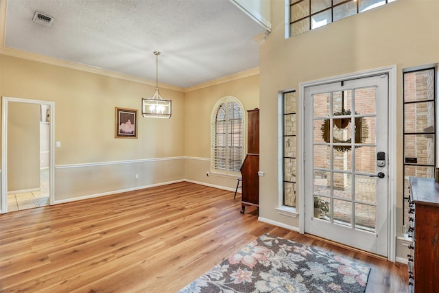 foyer entrance with ornamental molding, light hardwood / wood-style floors, a textured ceiling, and a notable chandelier