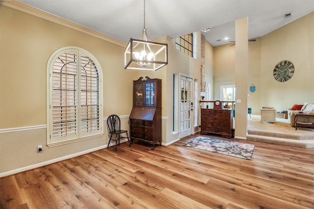 foyer featuring a notable chandelier, crown molding, light hardwood / wood-style floors, and a towering ceiling