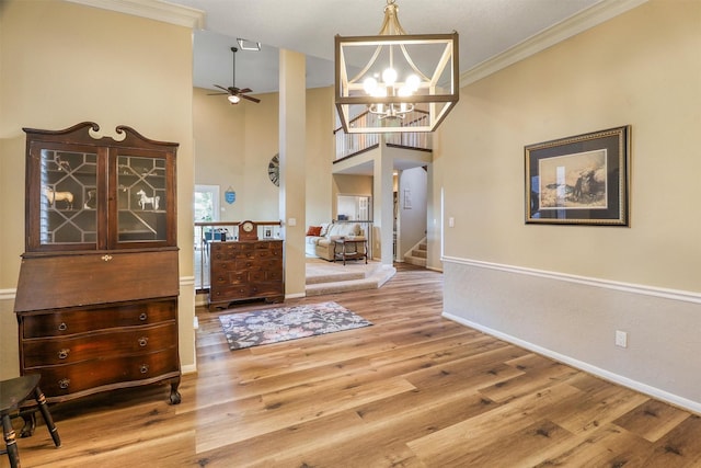 interior space with a high ceiling, crown molding, ceiling fan with notable chandelier, and hardwood / wood-style floors