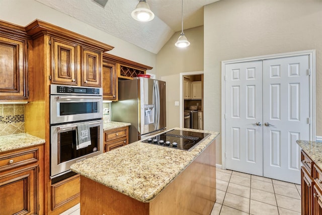 kitchen with stainless steel appliances, light stone countertops, washing machine and dryer, and a kitchen island