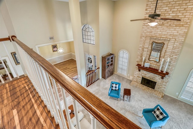 carpeted living room with a high ceiling, a brick fireplace, and ceiling fan