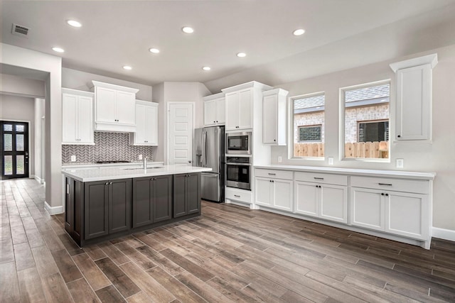 kitchen with white cabinetry, dark wood-type flooring, stainless steel appliances, and a center island with sink