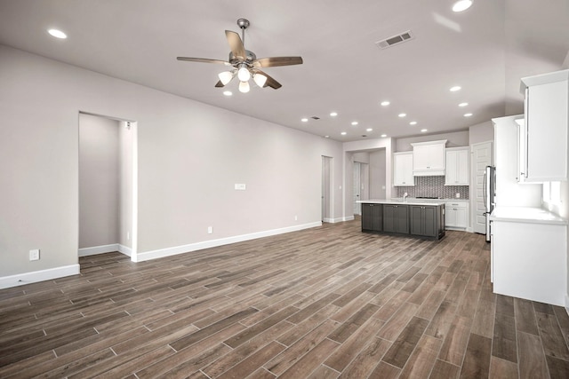 kitchen featuring white cabinetry, a center island with sink, stainless steel refrigerator, dark hardwood / wood-style floors, and backsplash