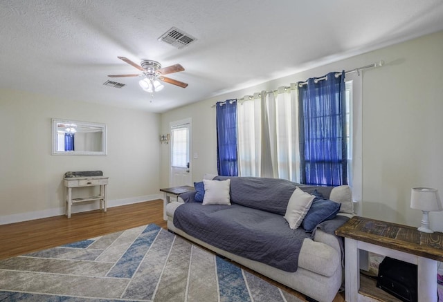 living room with a textured ceiling, wood-type flooring, and ceiling fan