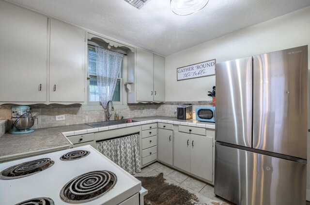 kitchen featuring tasteful backsplash, white cabinetry, sink, stainless steel fridge, and electric stove