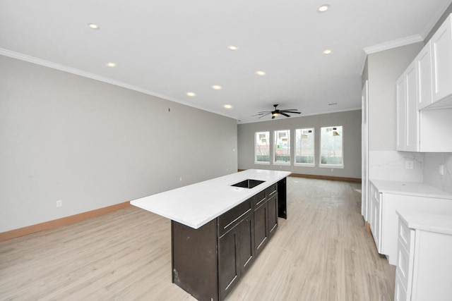 kitchen featuring crown molding, dark brown cabinetry, an island with sink, and light hardwood / wood-style flooring