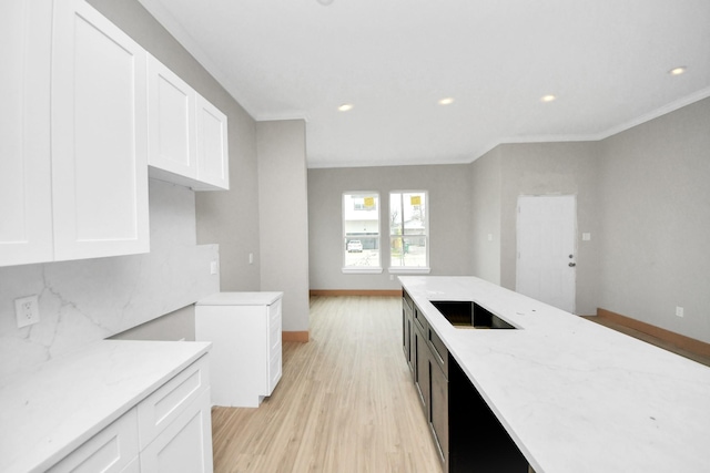 kitchen with light stone counters, light wood-type flooring, ornamental molding, decorative backsplash, and white cabinets