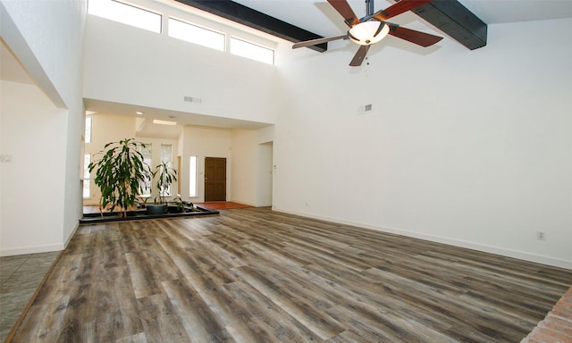 unfurnished living room with hardwood / wood-style floors, a towering ceiling, beamed ceiling, and ceiling fan