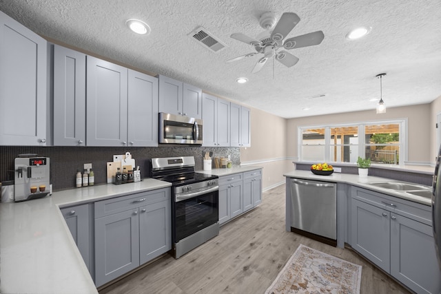 kitchen with appliances with stainless steel finishes, gray cabinetry, light hardwood / wood-style floors, and decorative light fixtures