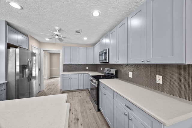 kitchen with ceiling fan, gray cabinetry, stainless steel appliances, decorative backsplash, and light wood-type flooring