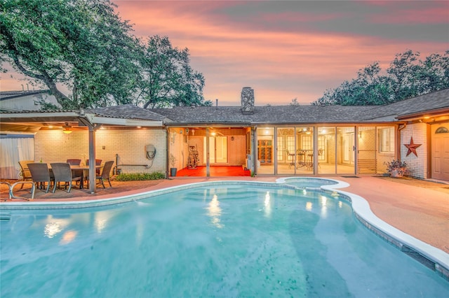 pool at dusk with a patio area and an in ground hot tub